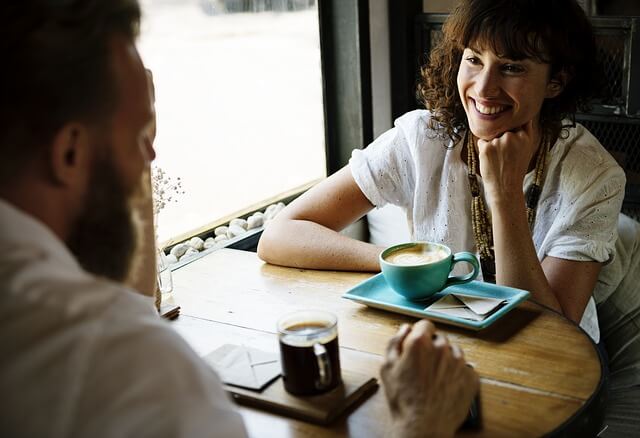 a professional looking man and woman smiling over cups of coffee inside a cafe